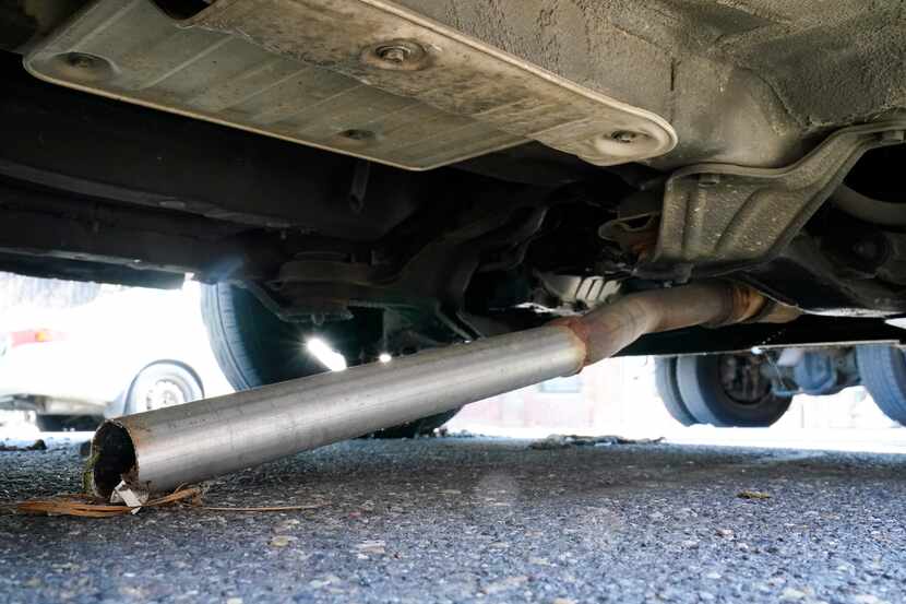 The exhaust pipe of an abandoned car missing its catalytic converter rests on the ground in...