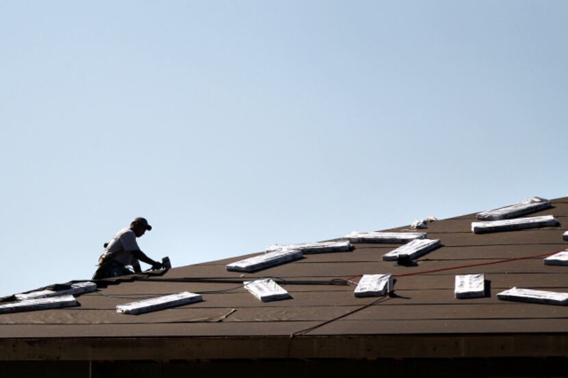 A construction worker applies shingles to the roof of a building under construction in...