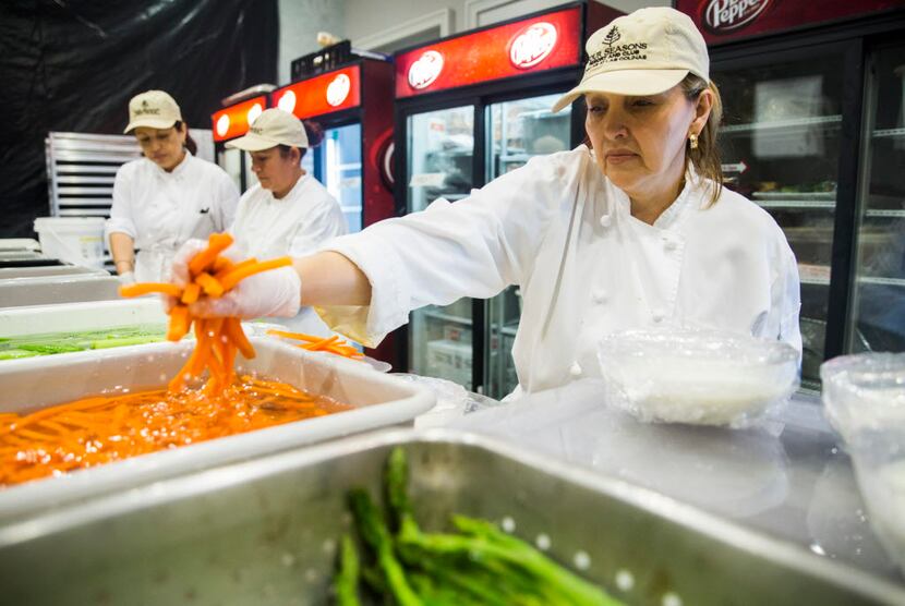 Kitchen staffer Teresa Castellanos reaches for a handful of carrots while assembling a...