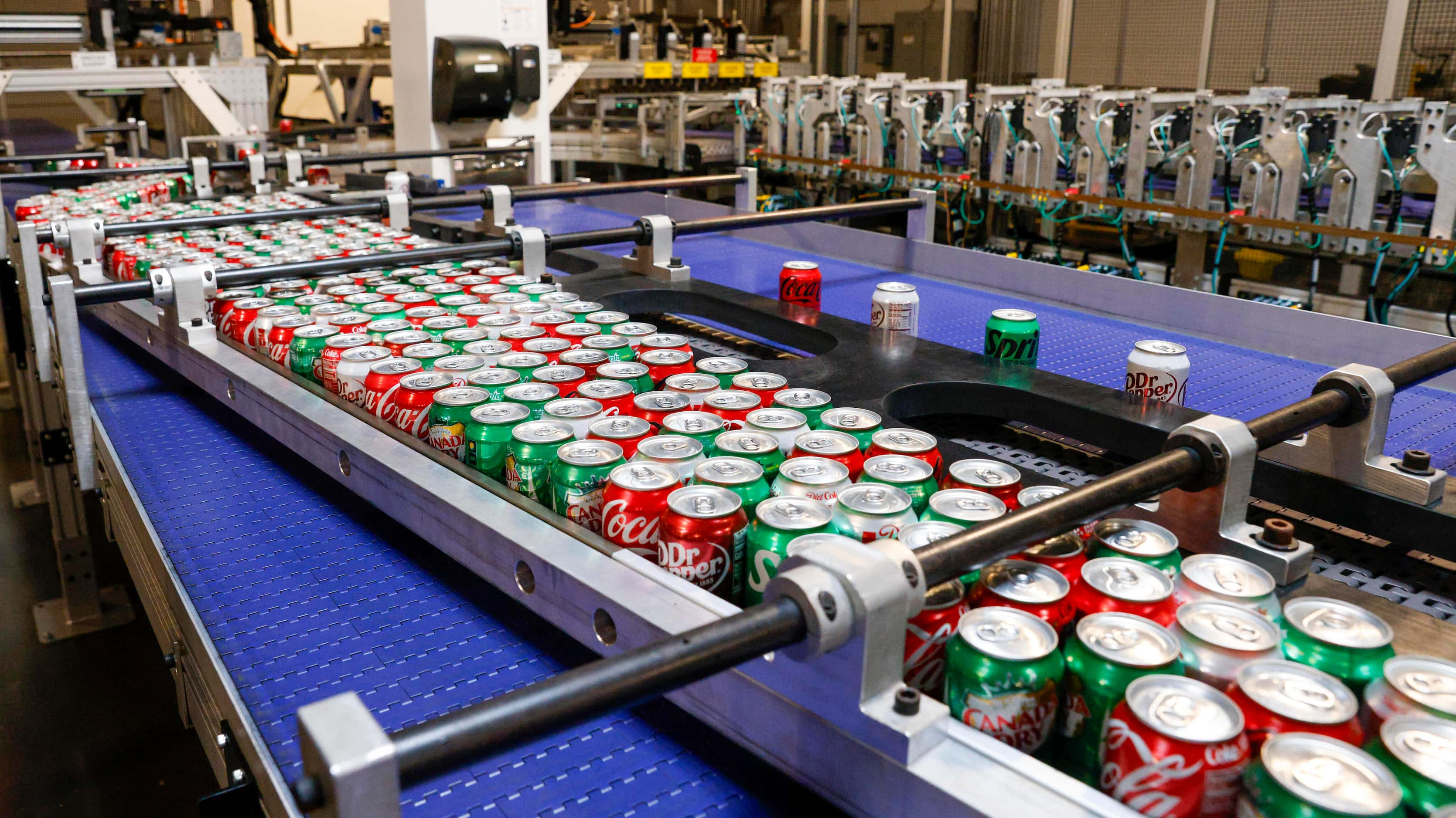 An automated machine sorts thousands of soda cans and loads them onto trays for aircraft at...