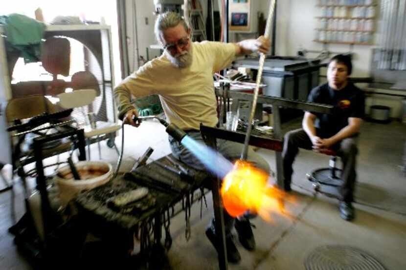 Jim Bowman, left, shapes a piece of molten glass as assistant Alberto Reyes looks on in...