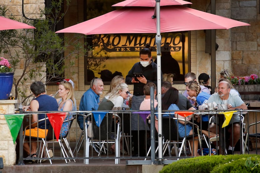A waiter wearing a face mask takes orders from diners eating on the outdoor patio at Rio...