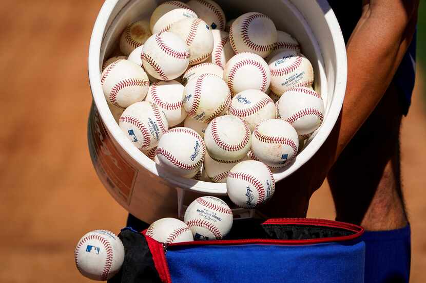 A Texas Rangers player dumps a bucket of baseballs from infield practice into a bag during a...