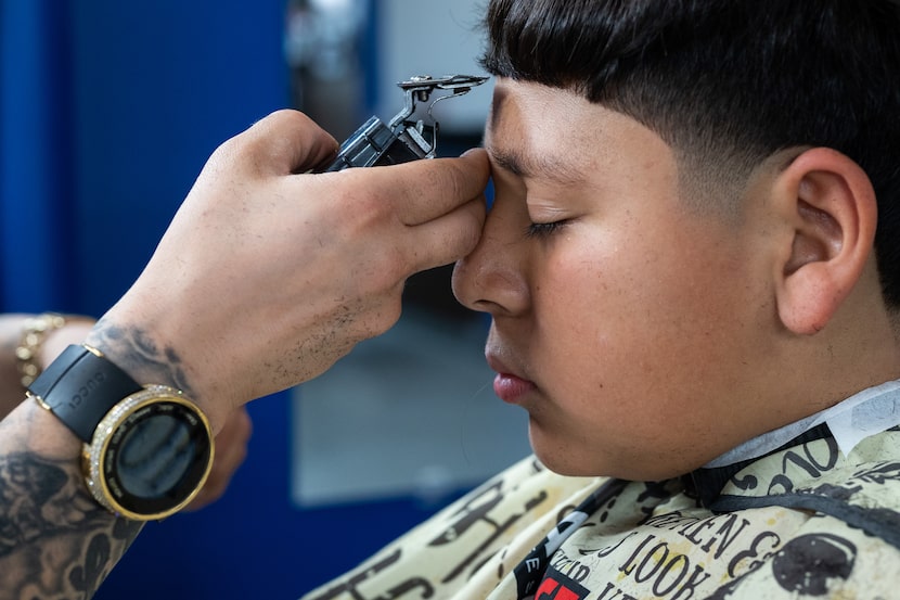 El barbero Edgar "E" Montelongo, de 35 años, corta el cabello de Nathan Cabrera, de 12,...