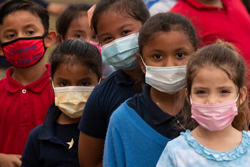 A group of first graders, wearing face masks, form a line to go back to class after recess...