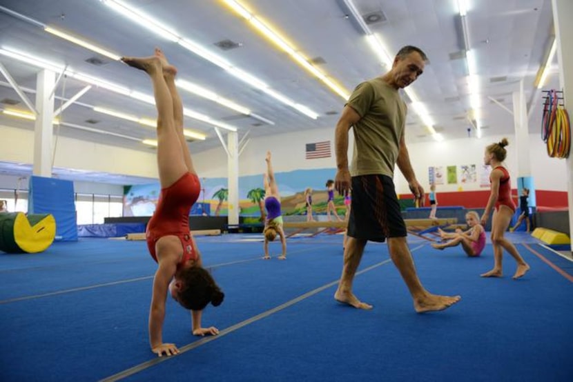 
Coach Eduoard Iarov walks past McCauley Harrington, 8, as she does a hand stand during an...