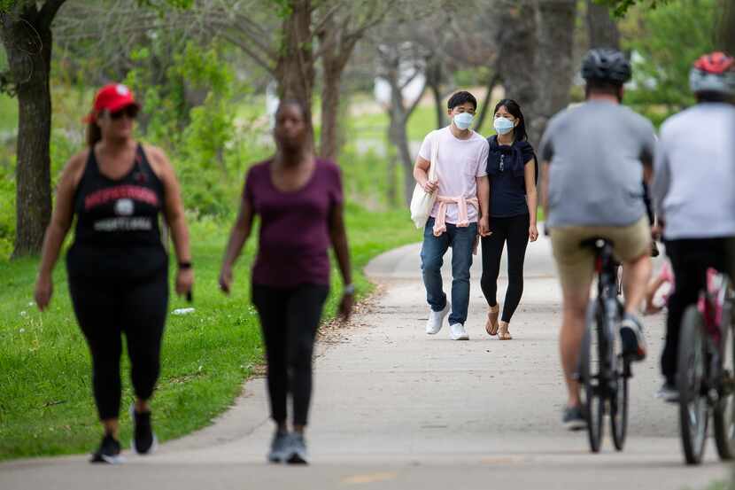 Will Kwon (center left) and Eunsol Noh wear masks as they walk at White Rock Lake on March...