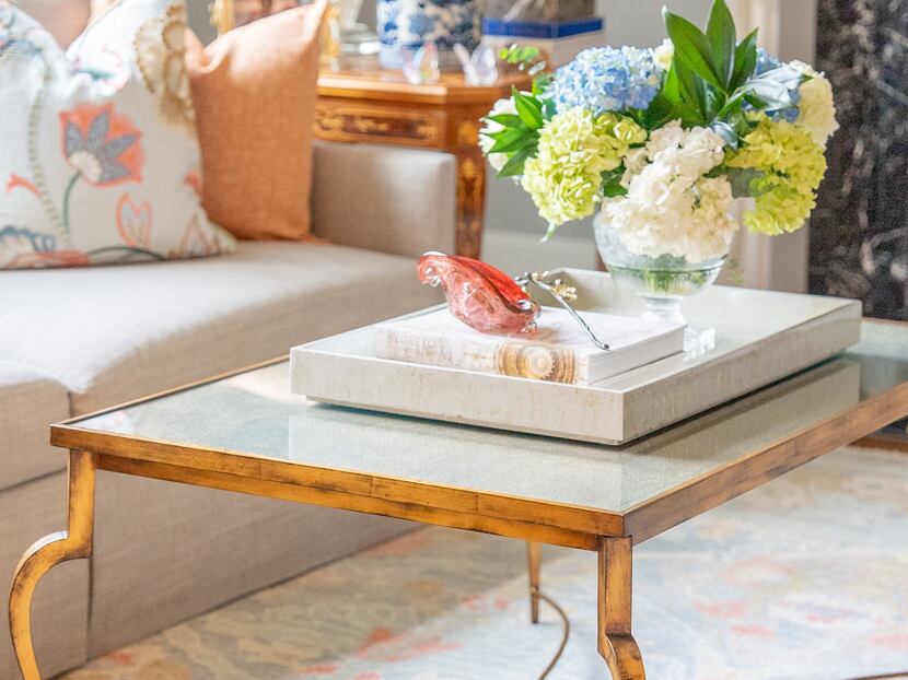 A gold coffee table is styled with a white tray.