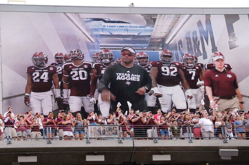 Fans in the upper deck cheer as the Aggies take the field, as seen on the giant electronic...