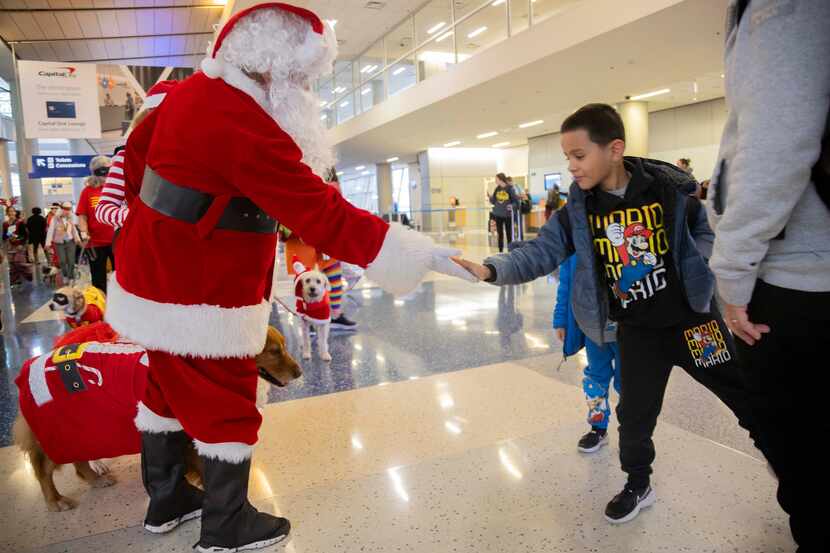 (From left) Dan Swanson dressed as Santa Claus greets Gabriel Mercado, 7, during the Holiday...