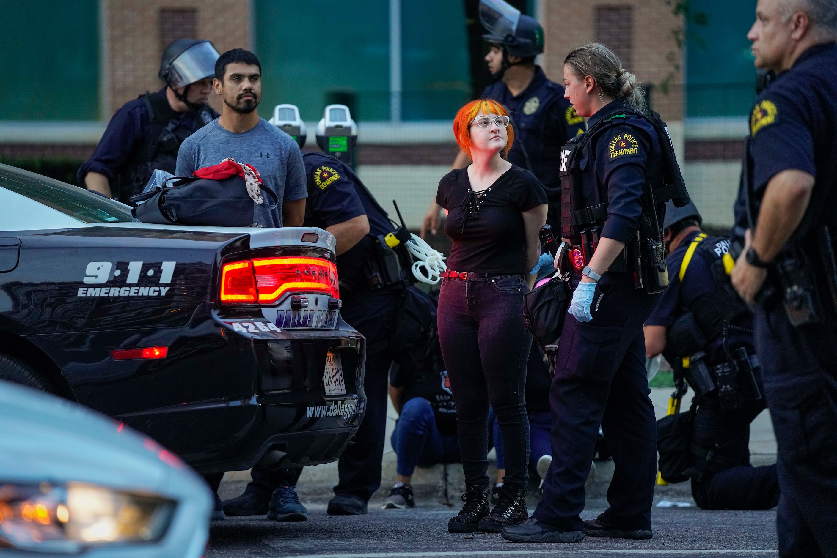 A group of people, some carrying protest signs, are arrested for curfew violations outside...