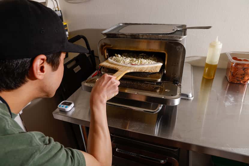 Peter Cho places a cheese pizza in one of two industrial ovens in his apartment kitchen in...