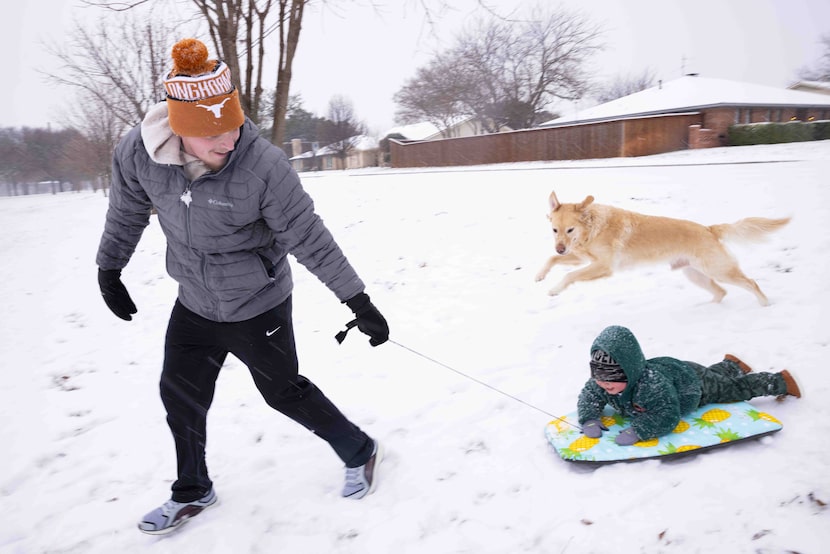 Tommy Tomlin of Plano leads his son Aiden, 2, down a snowy hill as dog Milo chases behind at...