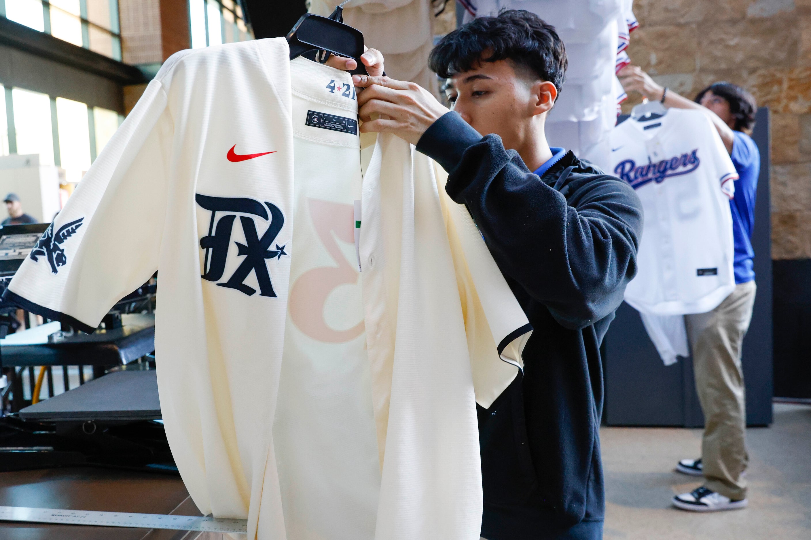 Eddy Briseno (center) prepares a Texas Rangers City Connect jersey for a customer before a...