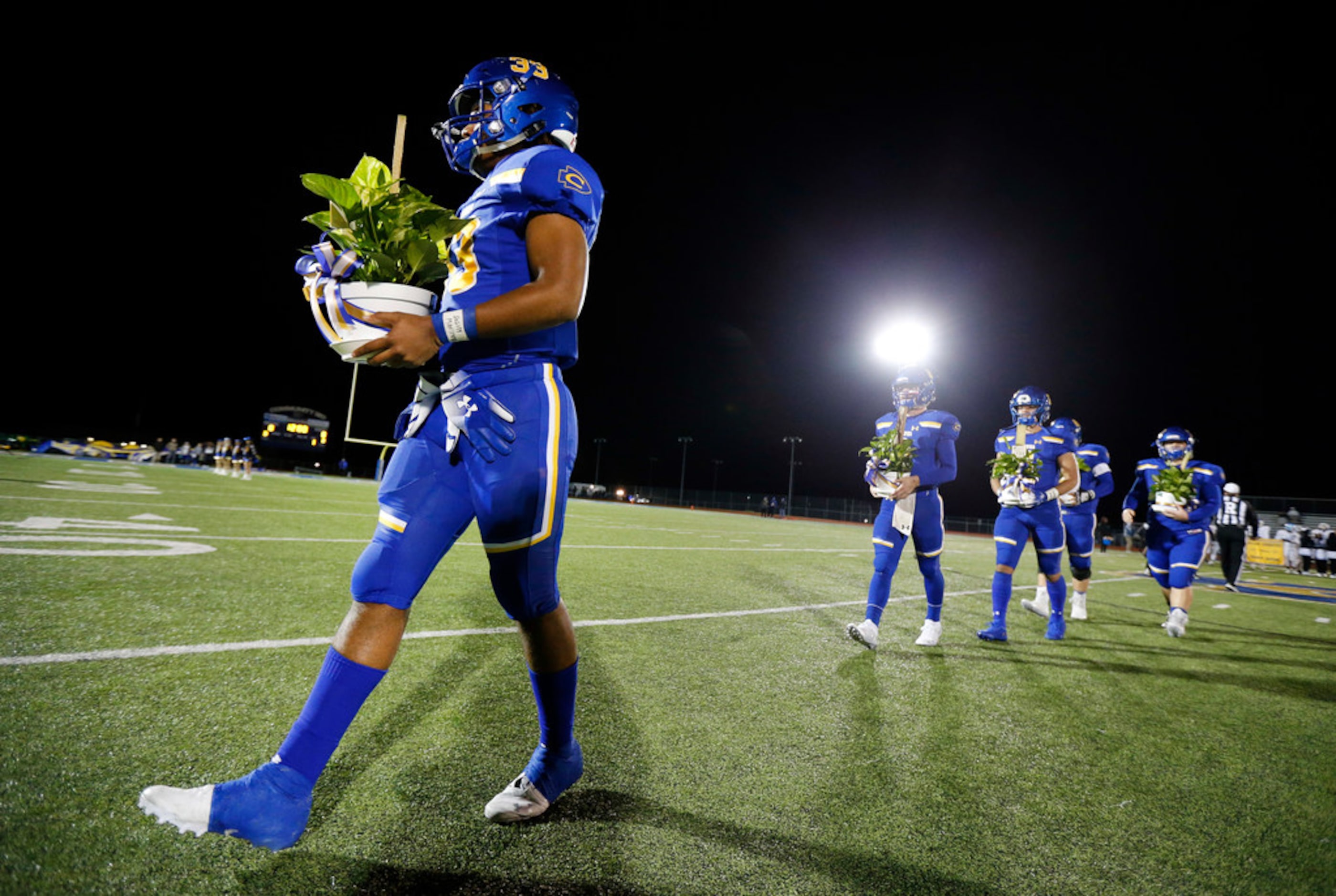 Community High defensive lineman Sean Outlaw (left) and his fellow captains carry plants...