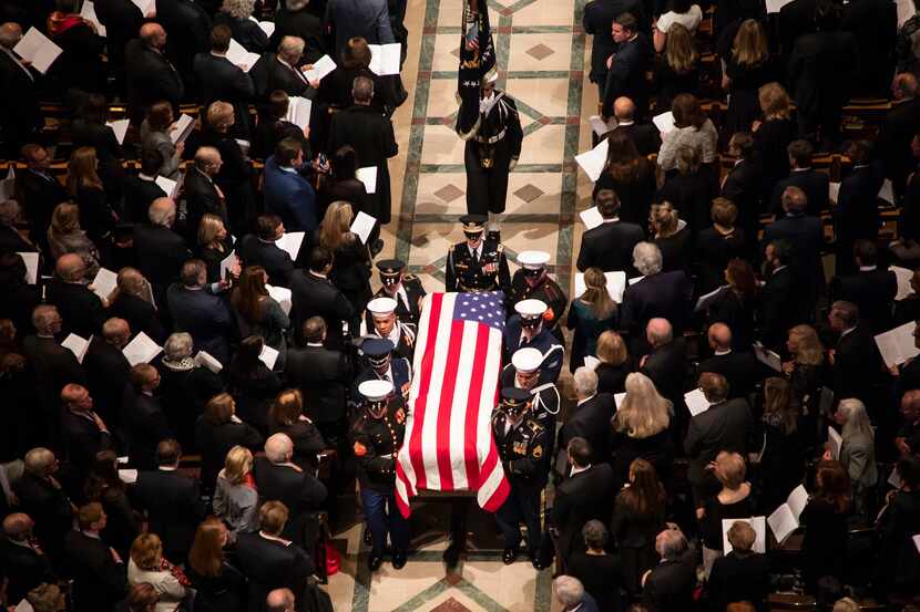 A military honor guard carries the flag-draped casket as it depart the Washington National...