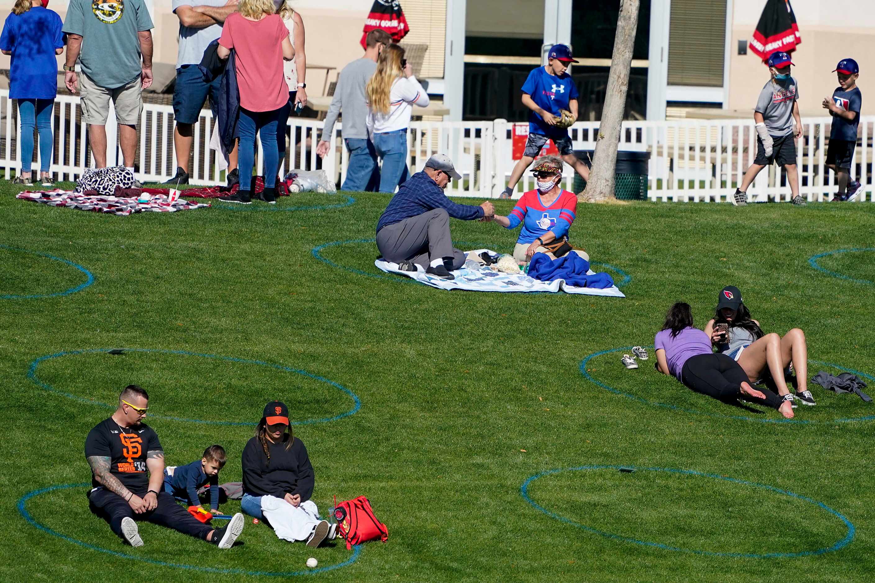 Fans on the outfield lawn sit in socially distant circles during the sixth inning of a...