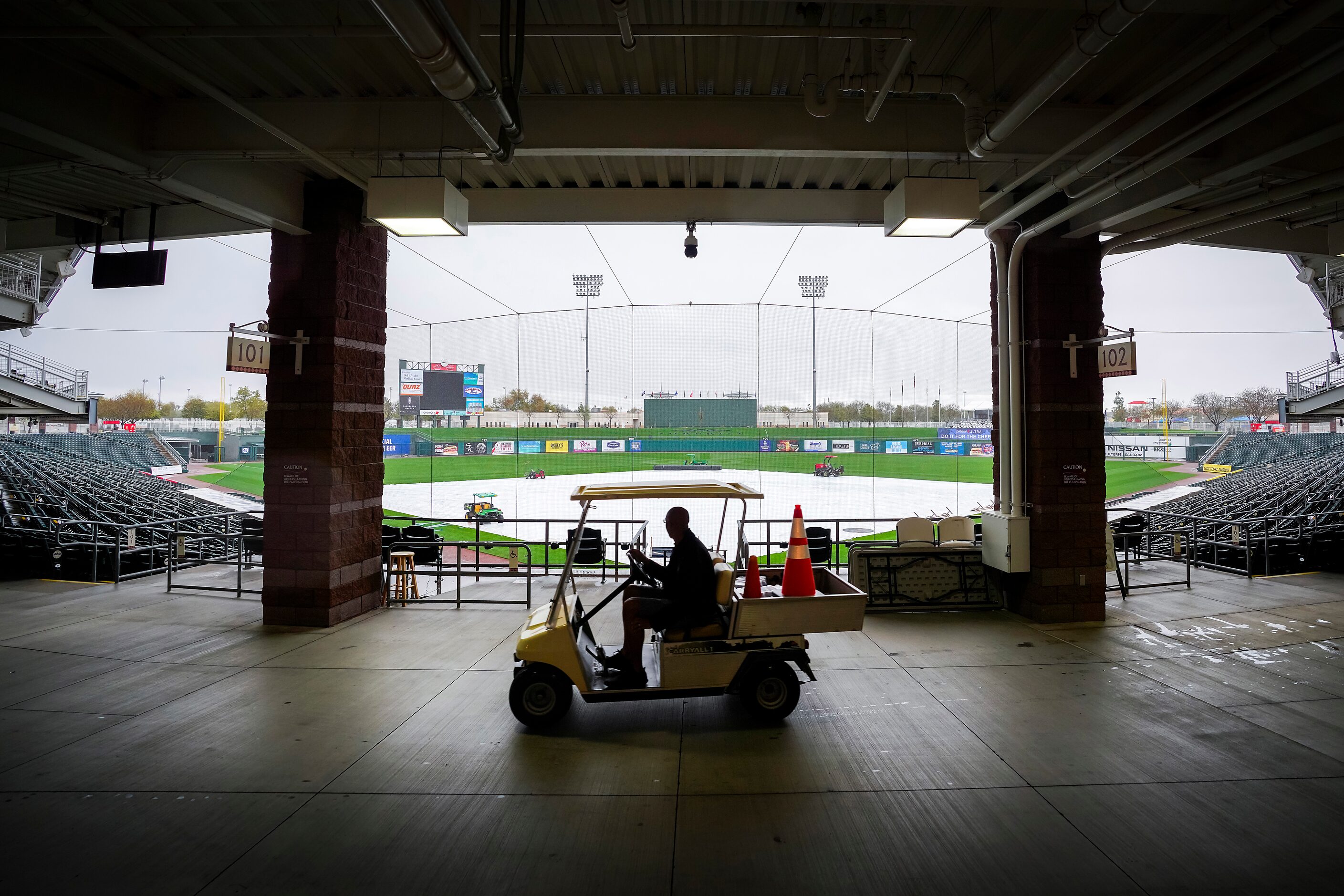 A stadium worker drives a cart through Surprise Stadium as tarp covers the field while rain...