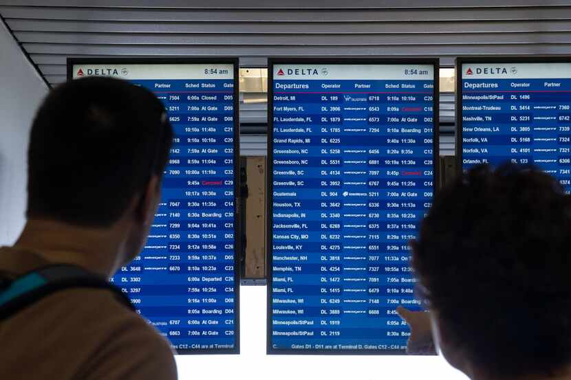 Travelers check a Delta departure board at New York's LaGuardia Airport for canceled or...