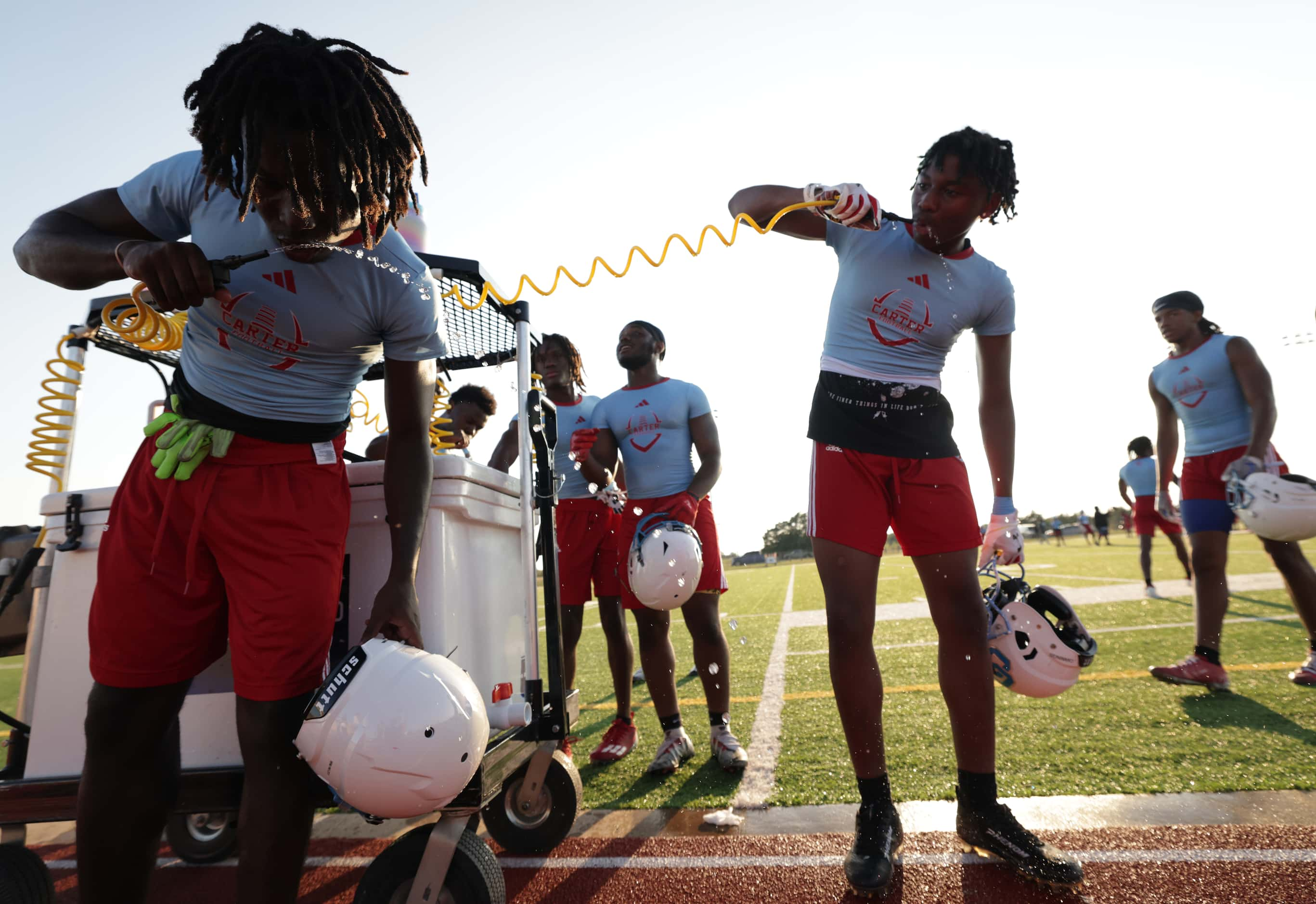 Players get a drink as they attend their first day of football practice at Carter High...