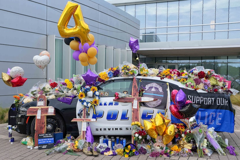 A pile of flowers, balloons and other mementos covers a Dallas police patrol car serving as...