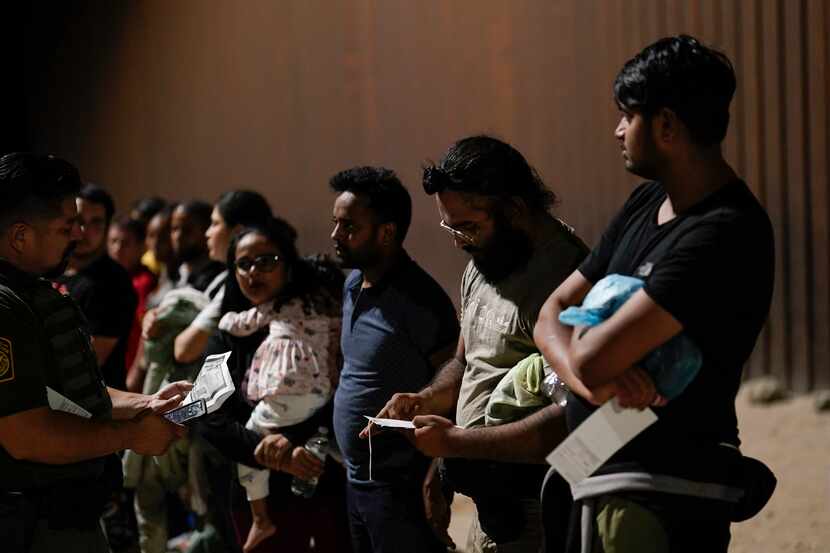 Migrantes esperan las indicaciones de los agentes de la Patrulla Fronteriza cerca de un muro...