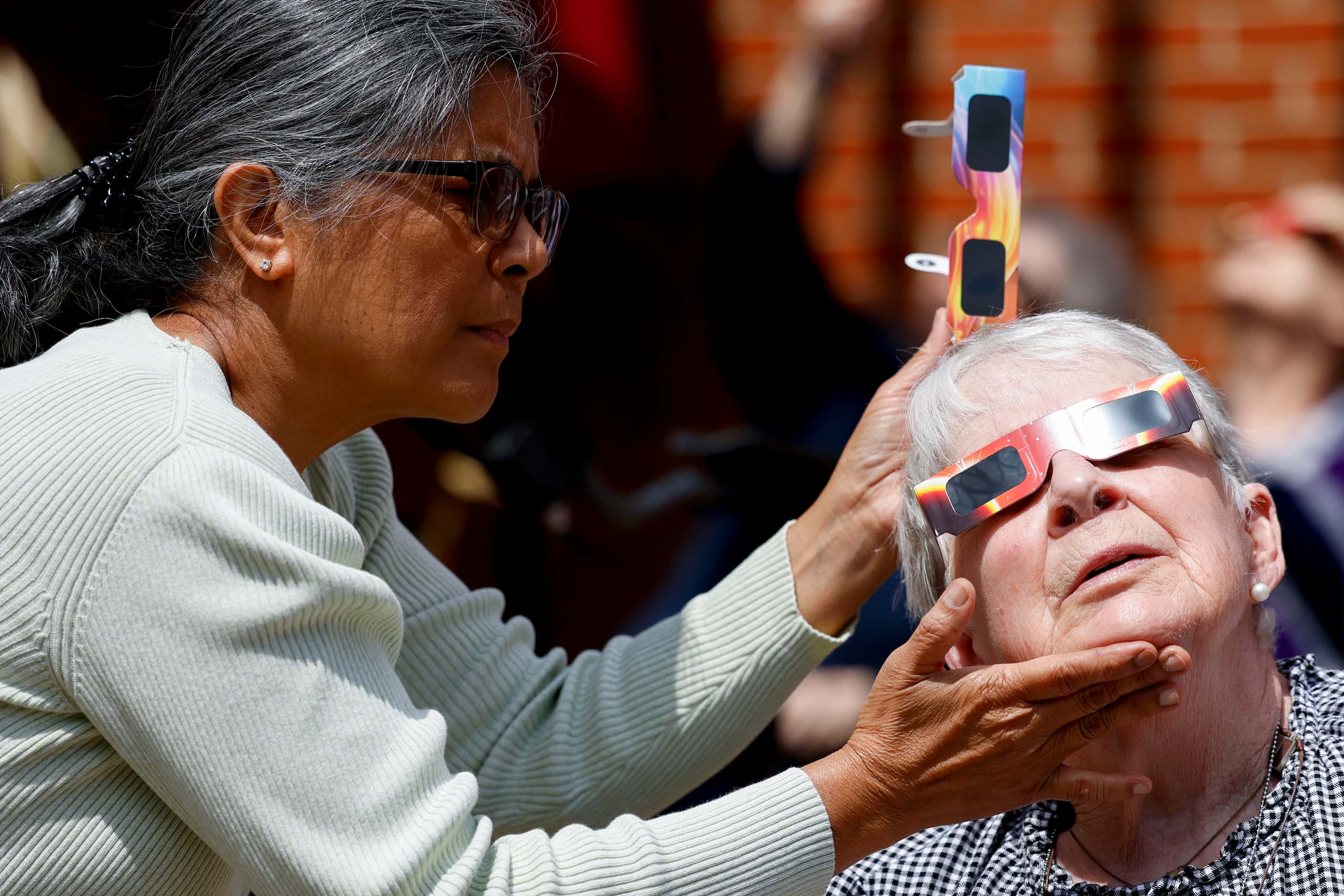 Gladys Cruz (left) helps resident Arlene Cleary with her eclipse glass as she tries to get a...