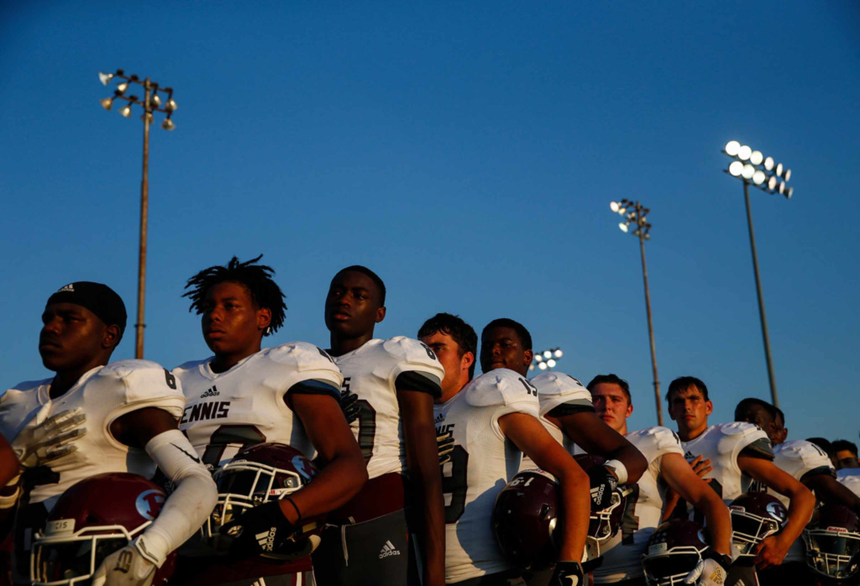 The Ennis Lions line up for the national anthem prior to a high school football game between...