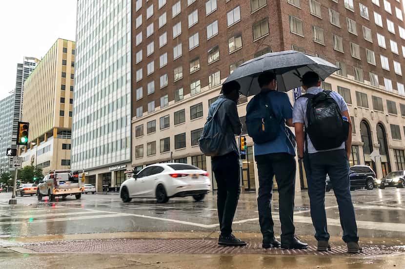 Pedestrians try to take cover from the rain as a thunderstorm rolls through downtown Dallas.