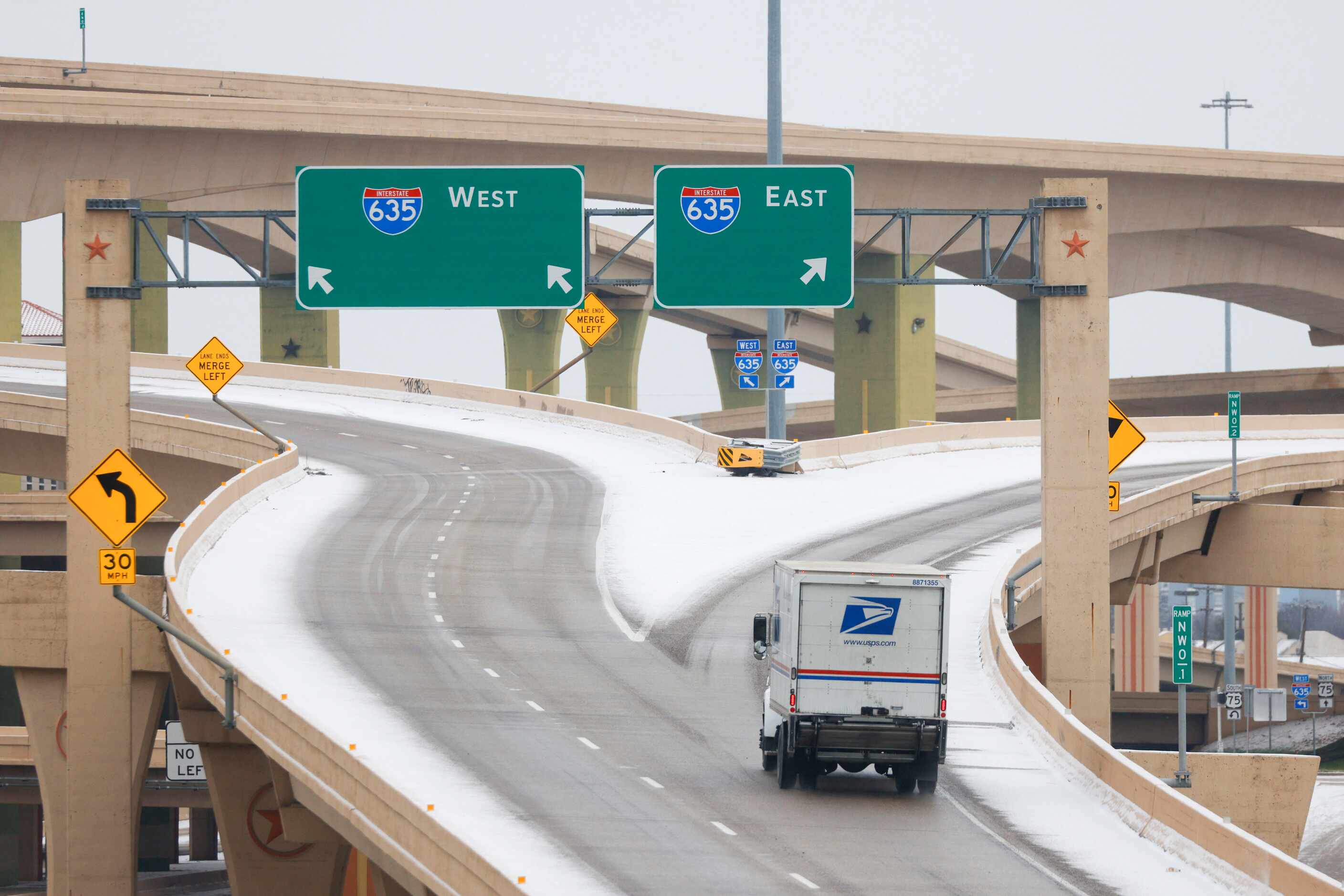 A USPS delivery truck travel through icy condition takes the Interstate 635 exit in High...