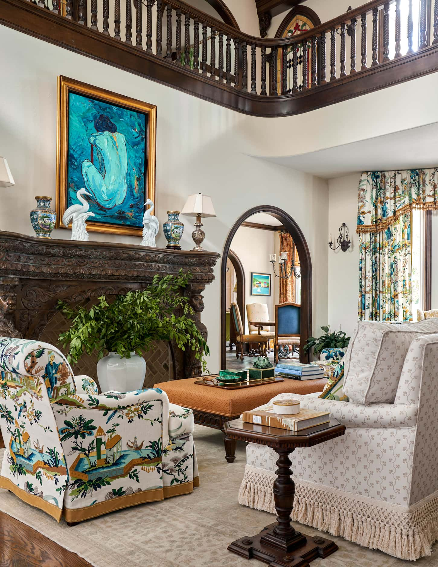 Armchairs, an ottoman and a sofa sit in front of a large fireplace where a blue painting...