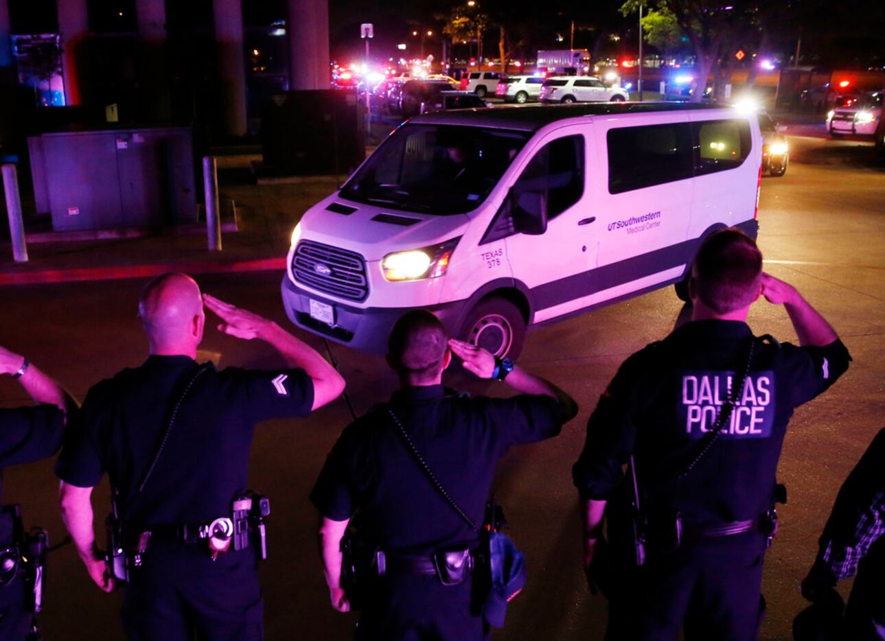Dallas police officers salute as the van carrying the body of slain officer Rogelio...
