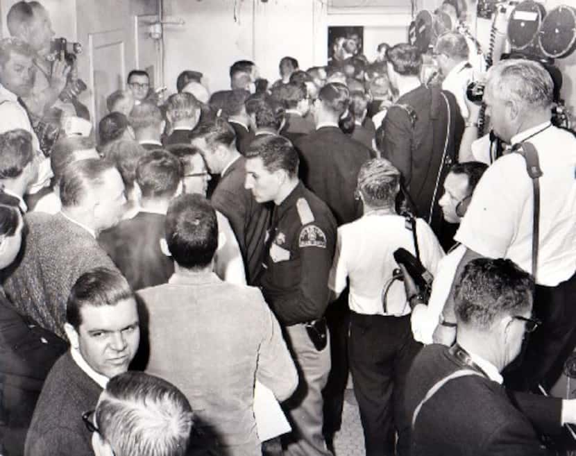 Law officers and members of the media wait outside a courtroom. 