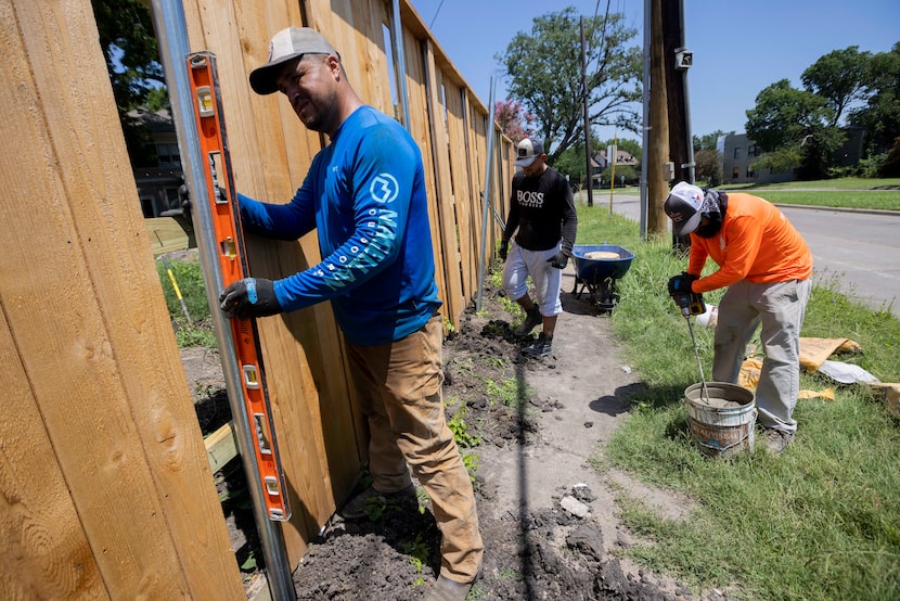 (From left) Contractor Gilberto Franco checks the leveling on a fence while working with...