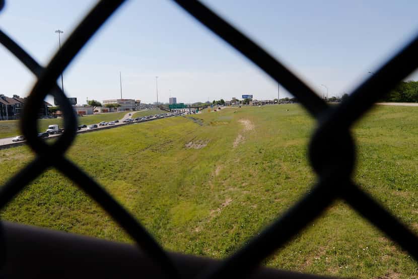 The chain link fence of a pedestrian bridge over LBJ Freeway frames undeveloped land on the...