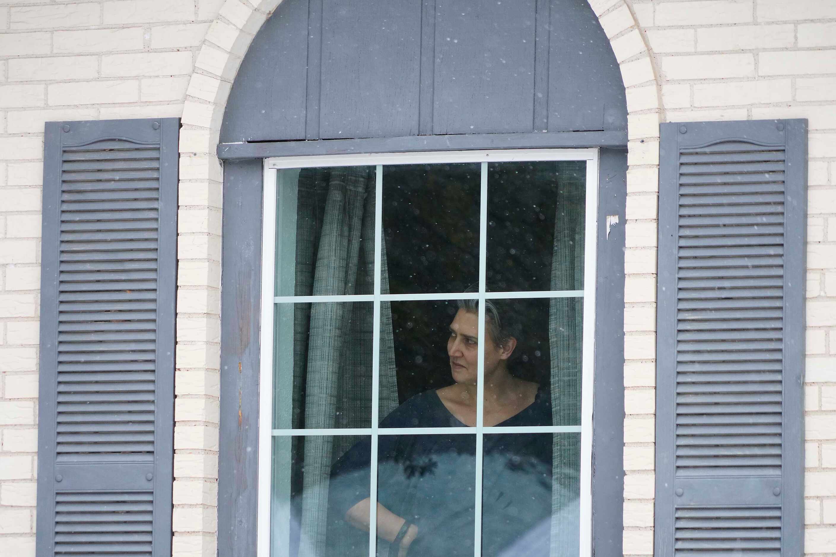 Liz Scrogginthorpe watches snow fall from her front window as her husband and children play...