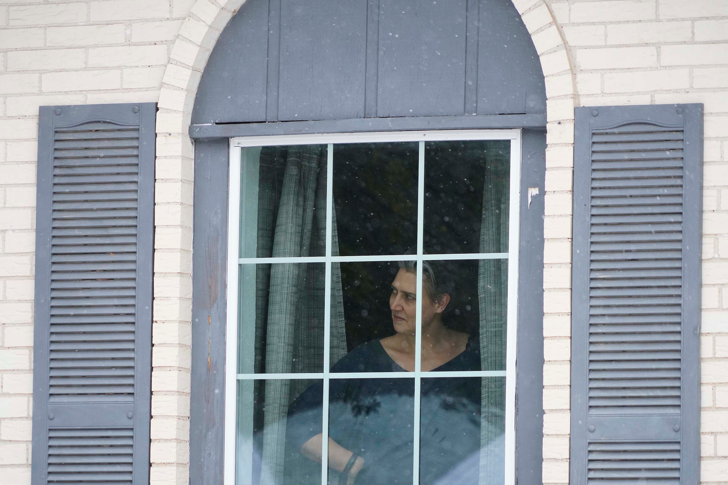 Liz Scrogginthorpe watches snow fall from her front window as her husband and children play...