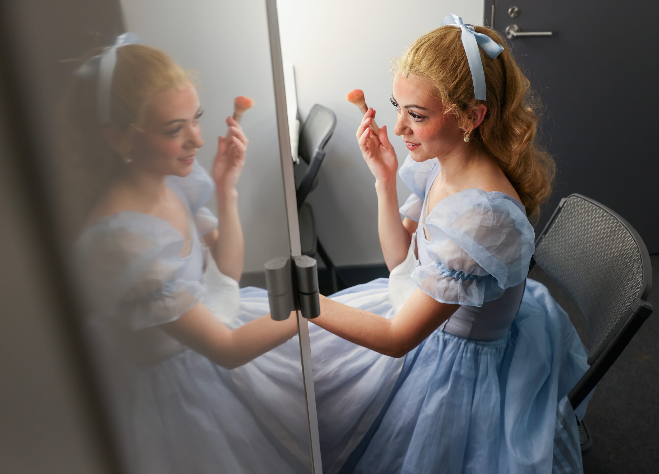 Alexandra F. Light brushes blush on her cheeks in front of the mirror of her dressing room...