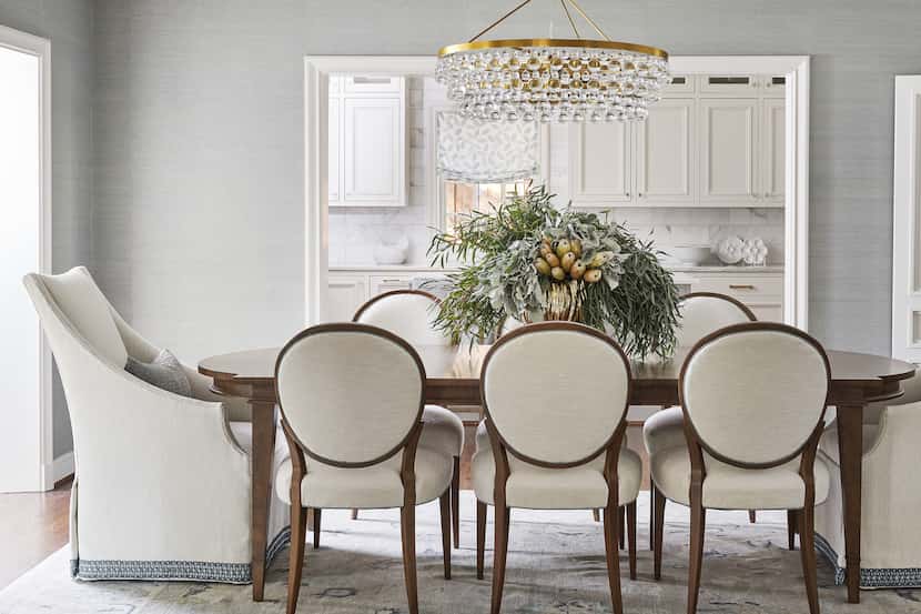A dining room with a crystal chandelier and white upholstered chairs
