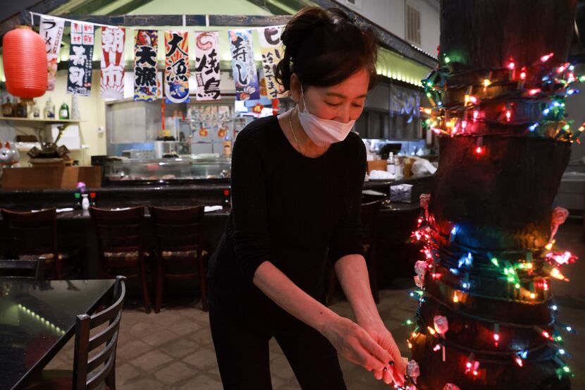 Sue Lee, co-owner and manager of Genroku Sushi & Grill, puts lollipops on a tree inside the...