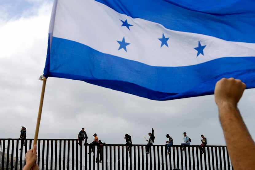 Migrantes centroamericanos se sientan en la parte superior del muro fronterizo el domingo 29...