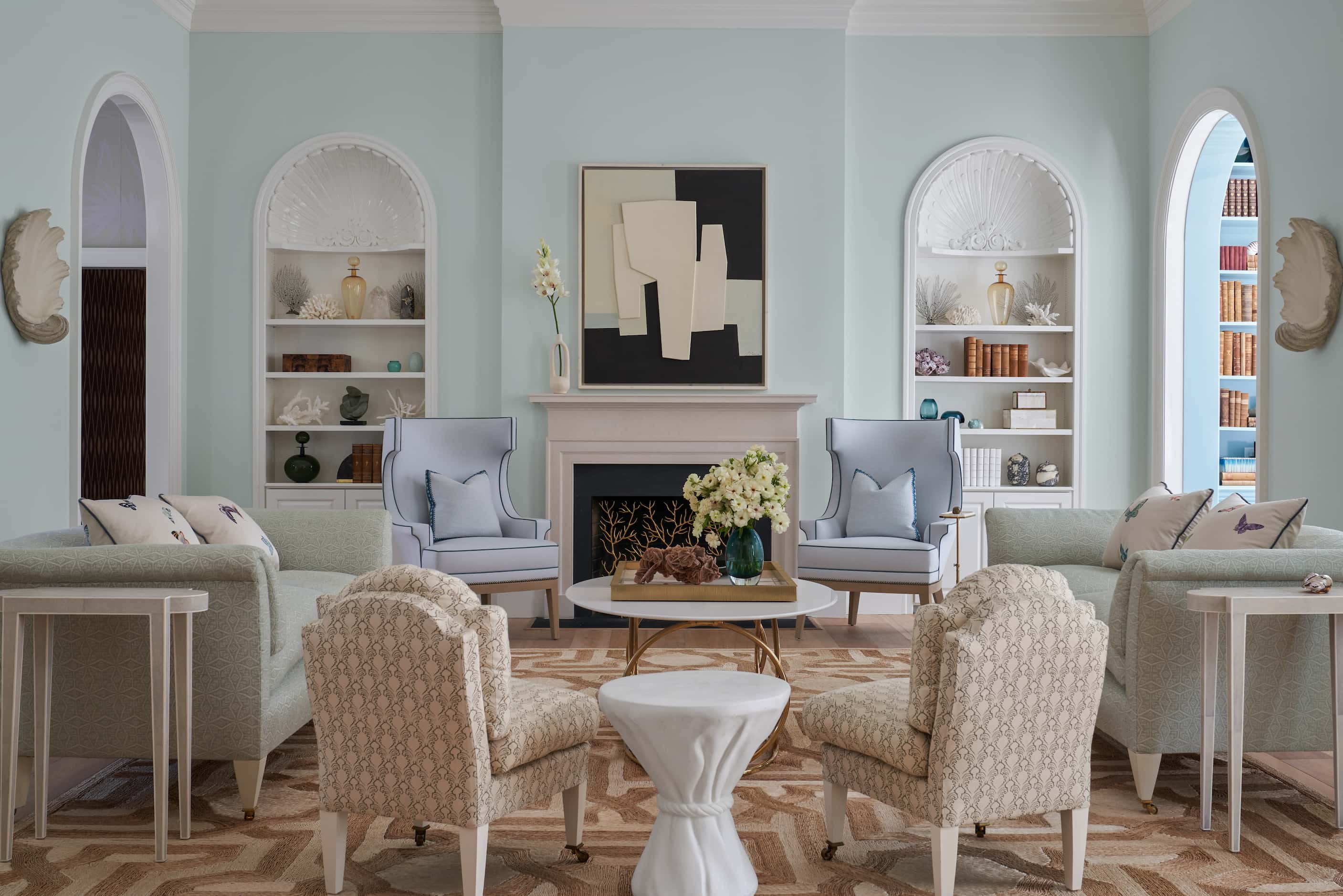 Pale blue living room with two sofas, two slipper chairs and two armchairs, cove bookshelves...