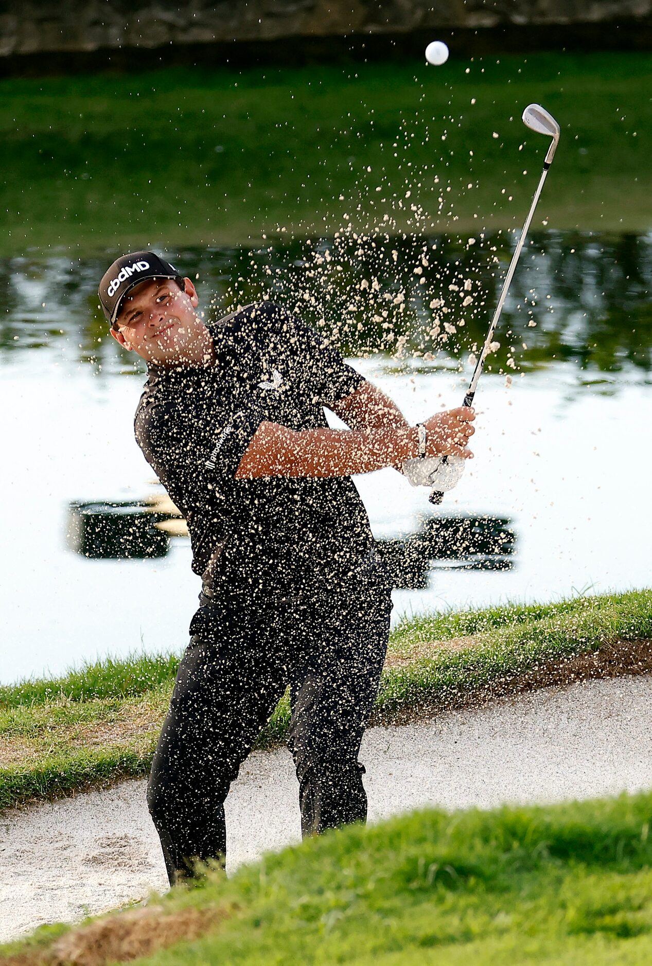 Professional golfer Patrick Reed splashes out of the No. 18 green side bunker during round...