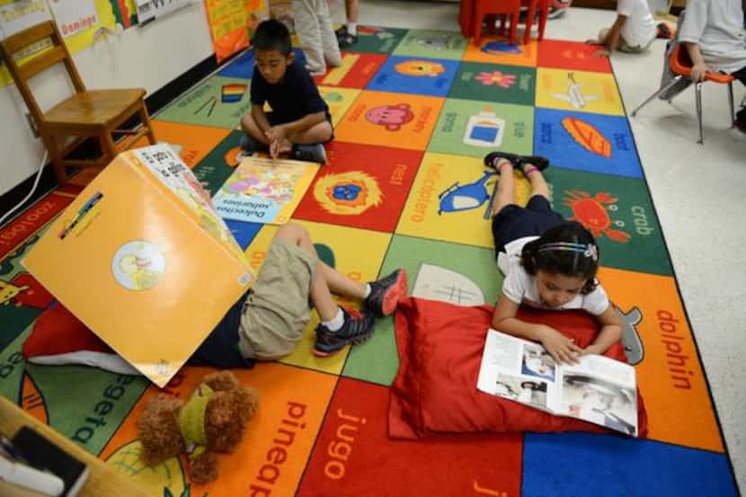 
Kindergartners read books in Spanish during class while laying on a mat that displays items...