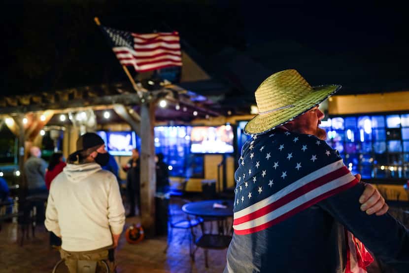 Elliot Fischer (right) wears a flag scarf as he joins others watching election results at...