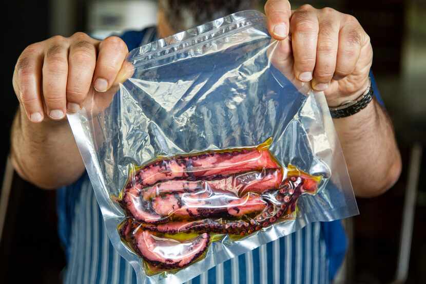 David Uygur holds up octopus tentacles in a vacuum-sealed sous vide bag at his restaurant,...