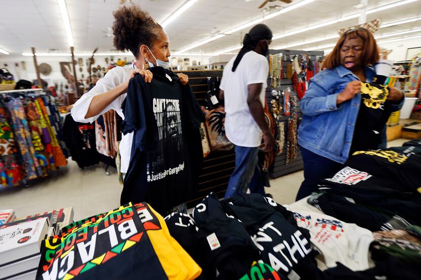 Shop owner Akwete Tyehimba (left) shows a new George Floyd 'I Can't Breathe' T-shirt to...