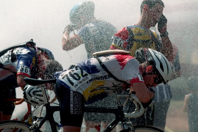 Exhausted cyclists cool  down  under the spray of a water hydrant after  completing the...