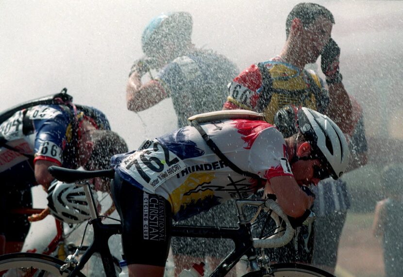 Exhausted cyclists cool  down  under the spray of a water hydrant after  completing the...