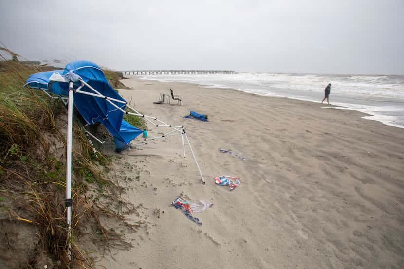 A person walks on a windy and rainy beach as Tropical Storm Debby approaches the area,...